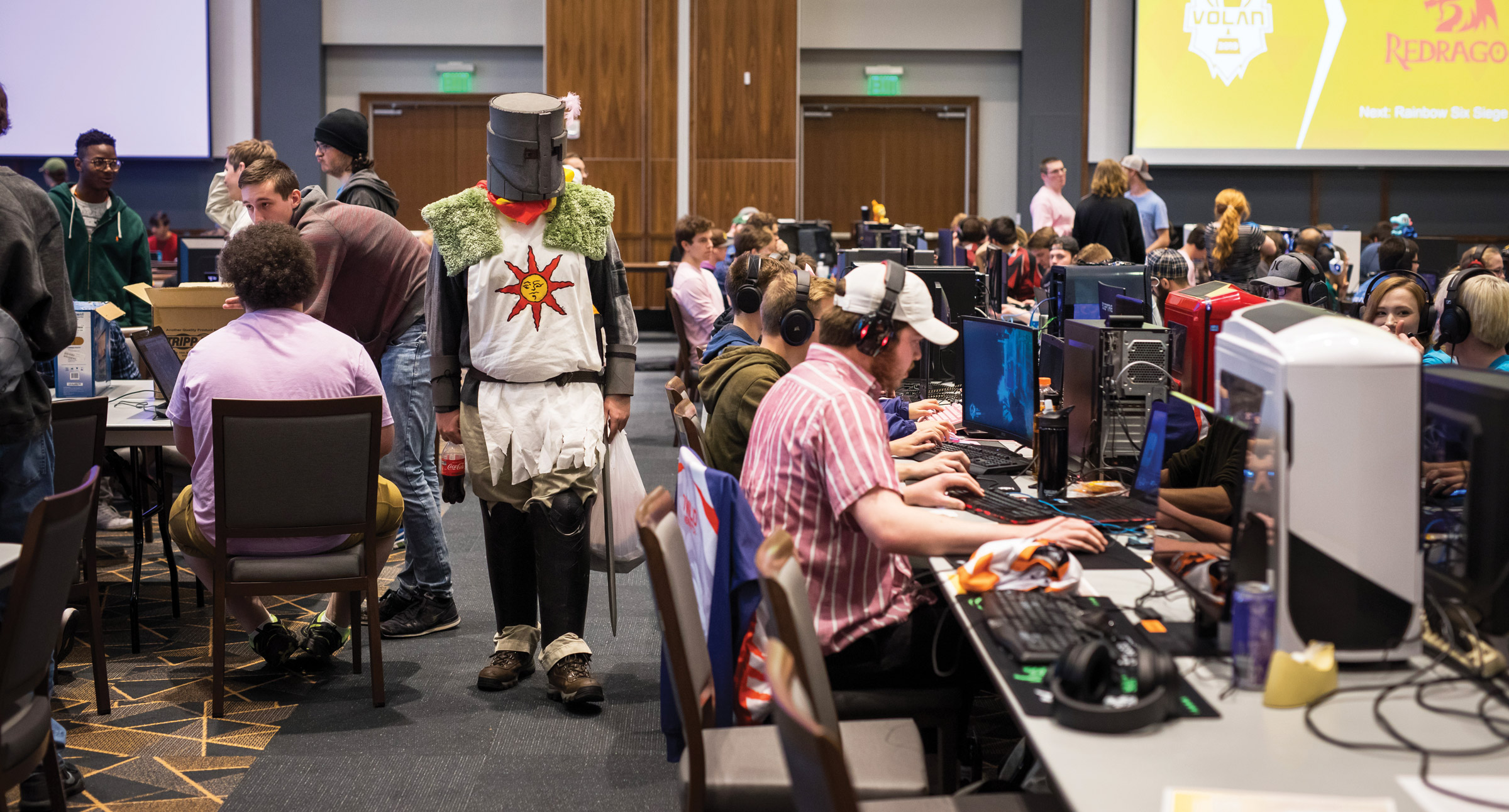 A student dressed as a knight walks between rows of gamers at PC consoles