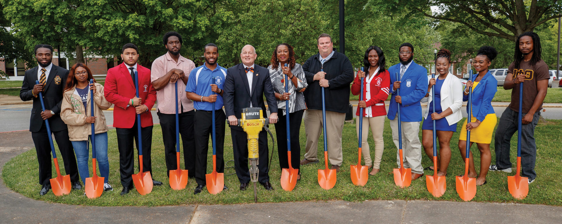 Chancellor Keith Carver holds a jackhammer in the center of a group of students and alumni representing their Divine Nine fraternities and sororities