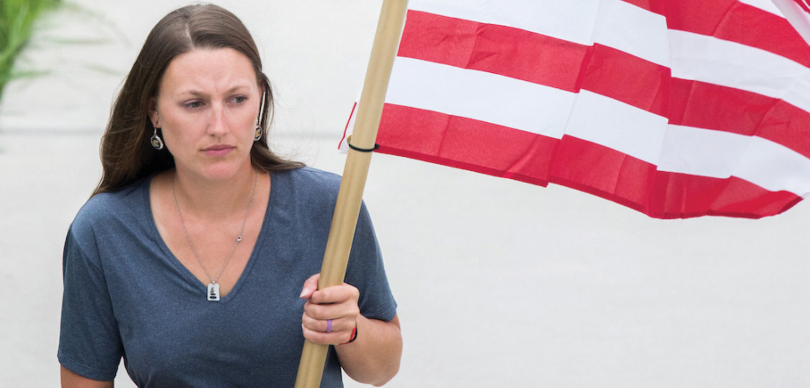 A woman carries the American flag across a walkway on UTCs campus. She is wearing a navy blue shirt and gold pants