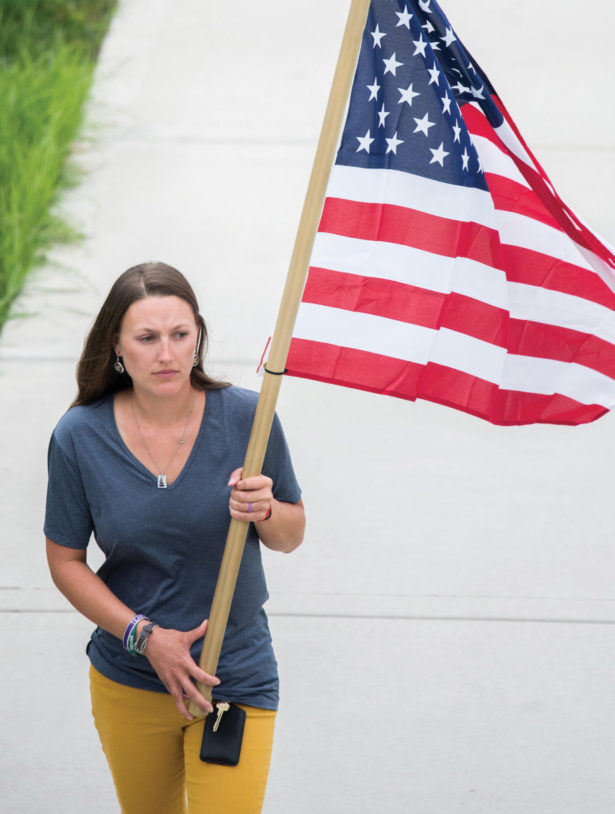 A woman carries the American flag across a walkway on UTCs campus. She is wearing a navy blue shirt and gold pants