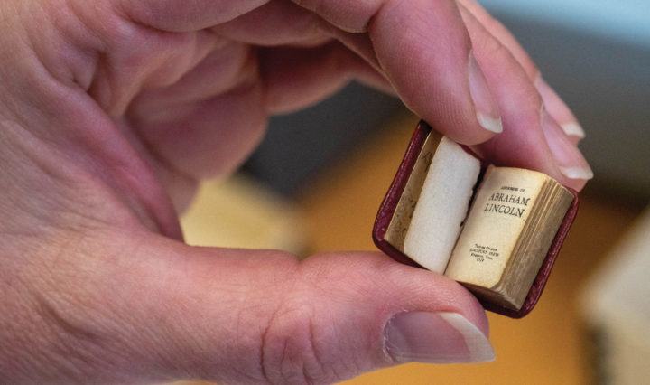 A tiny perfect bound leather book held between a thumb and index and middle fingers