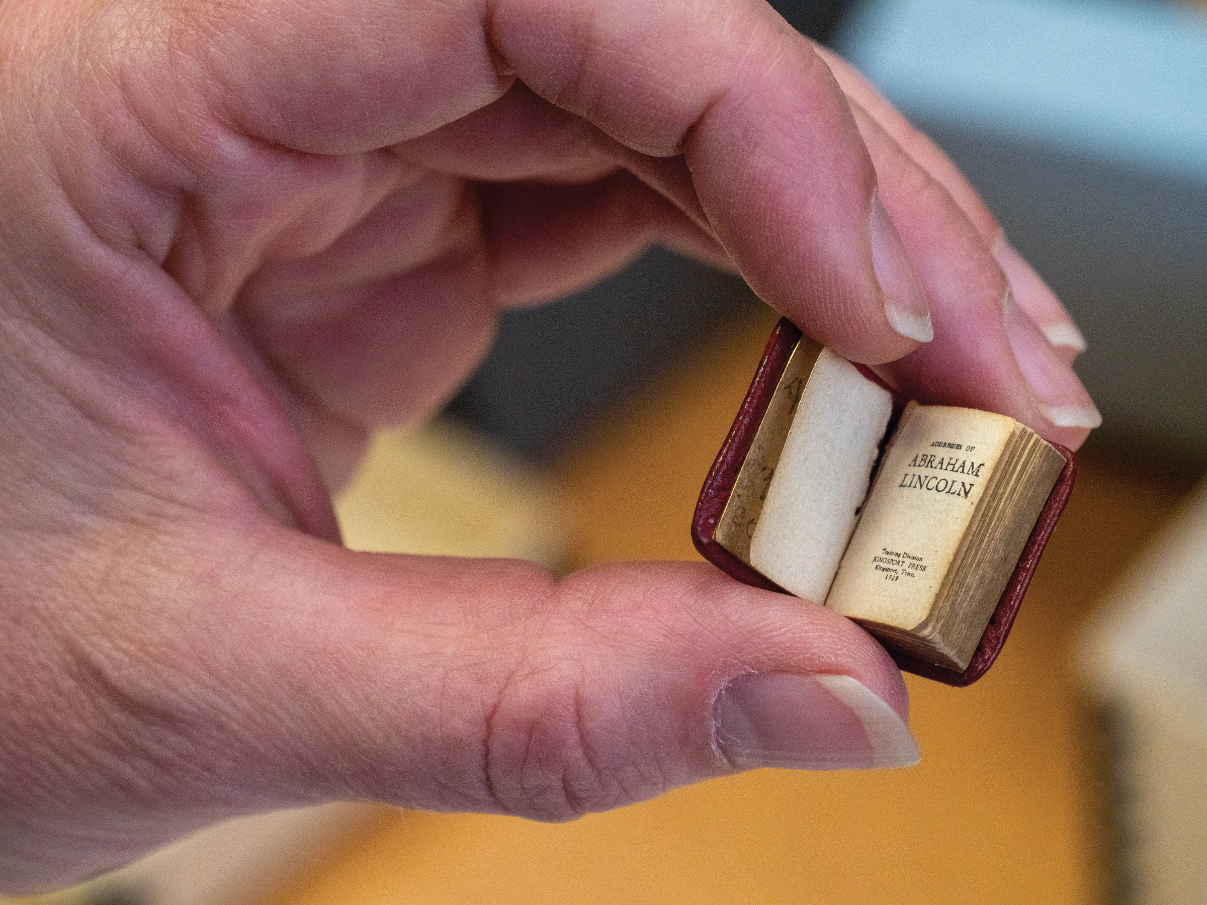 A tiny perfect bound leather book held between a thumb and index and middle fingers
