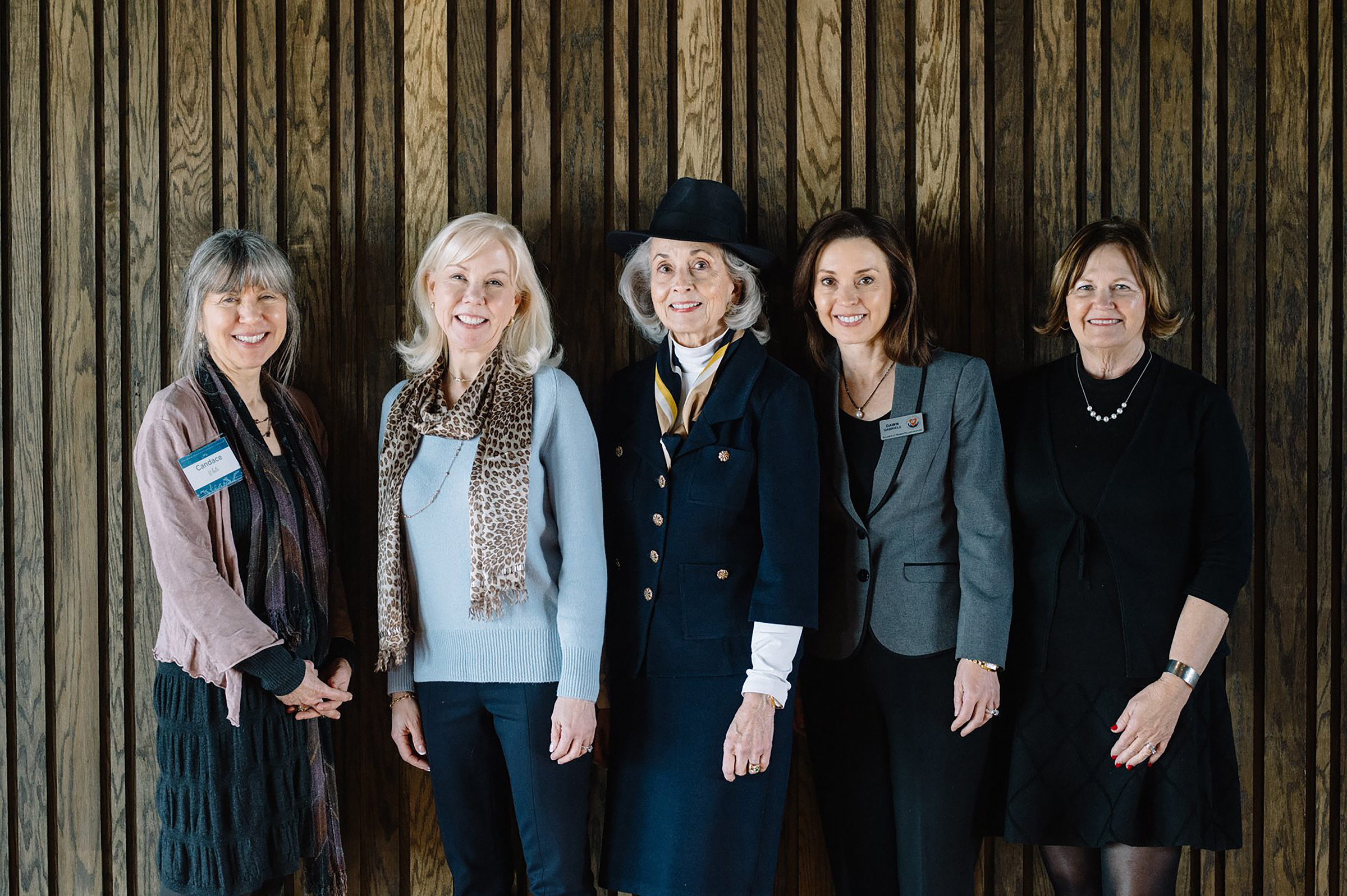 Five professionally dressed women stand together for a group photo