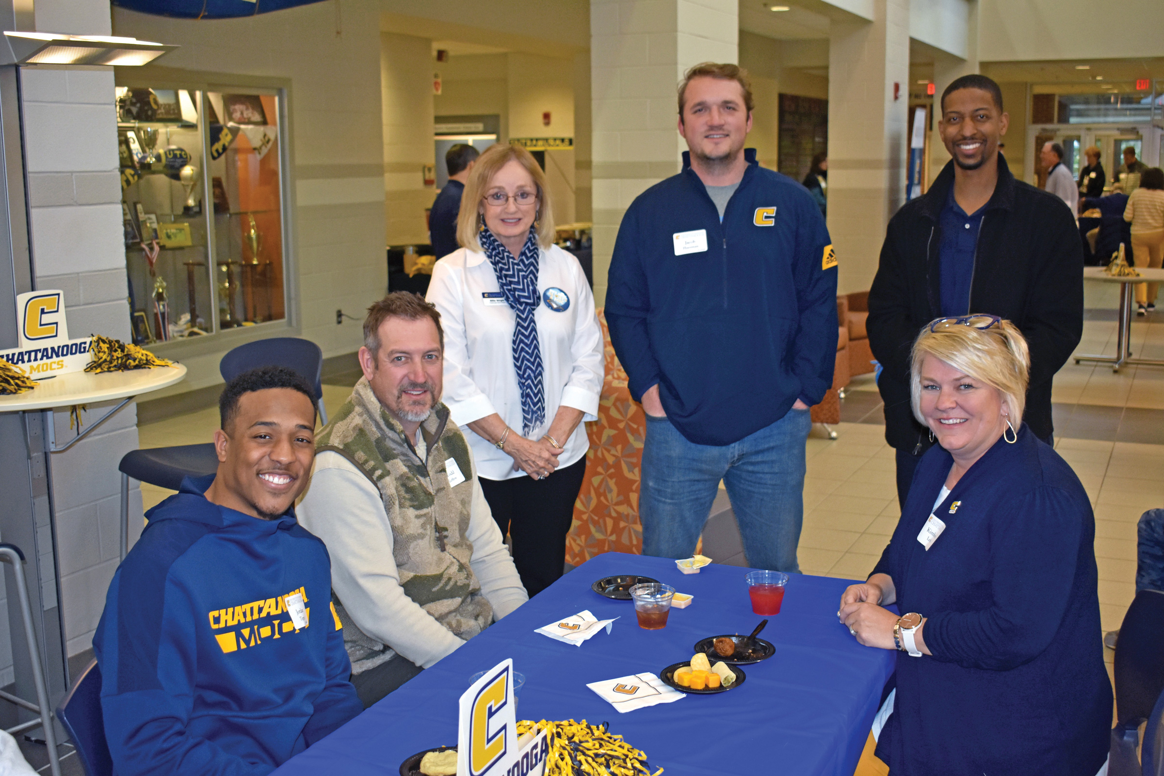 Five people stand around a table dressed in blue and gold