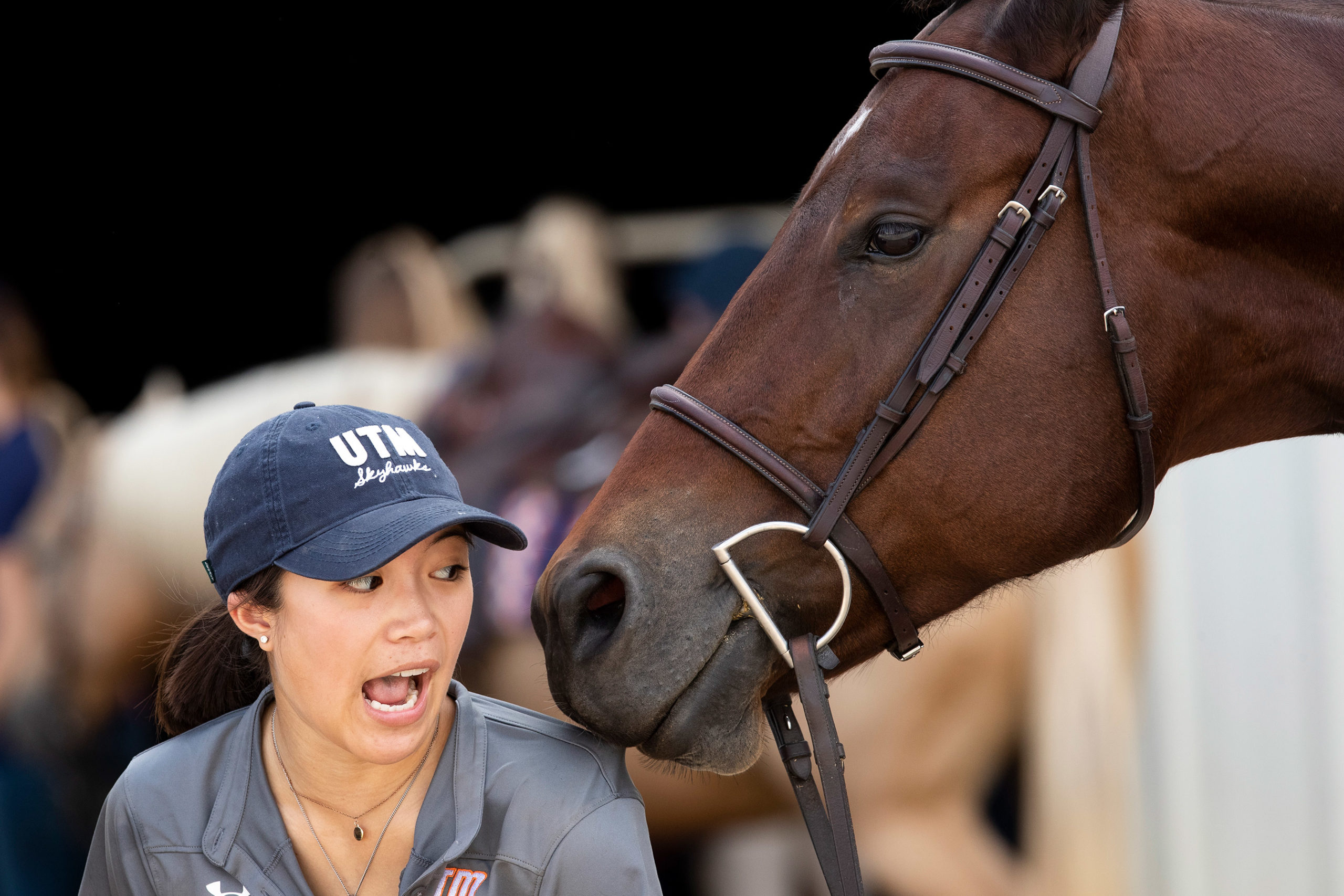 A chestnut horse displays affection with a young woman in a UTM Skyhawks cap