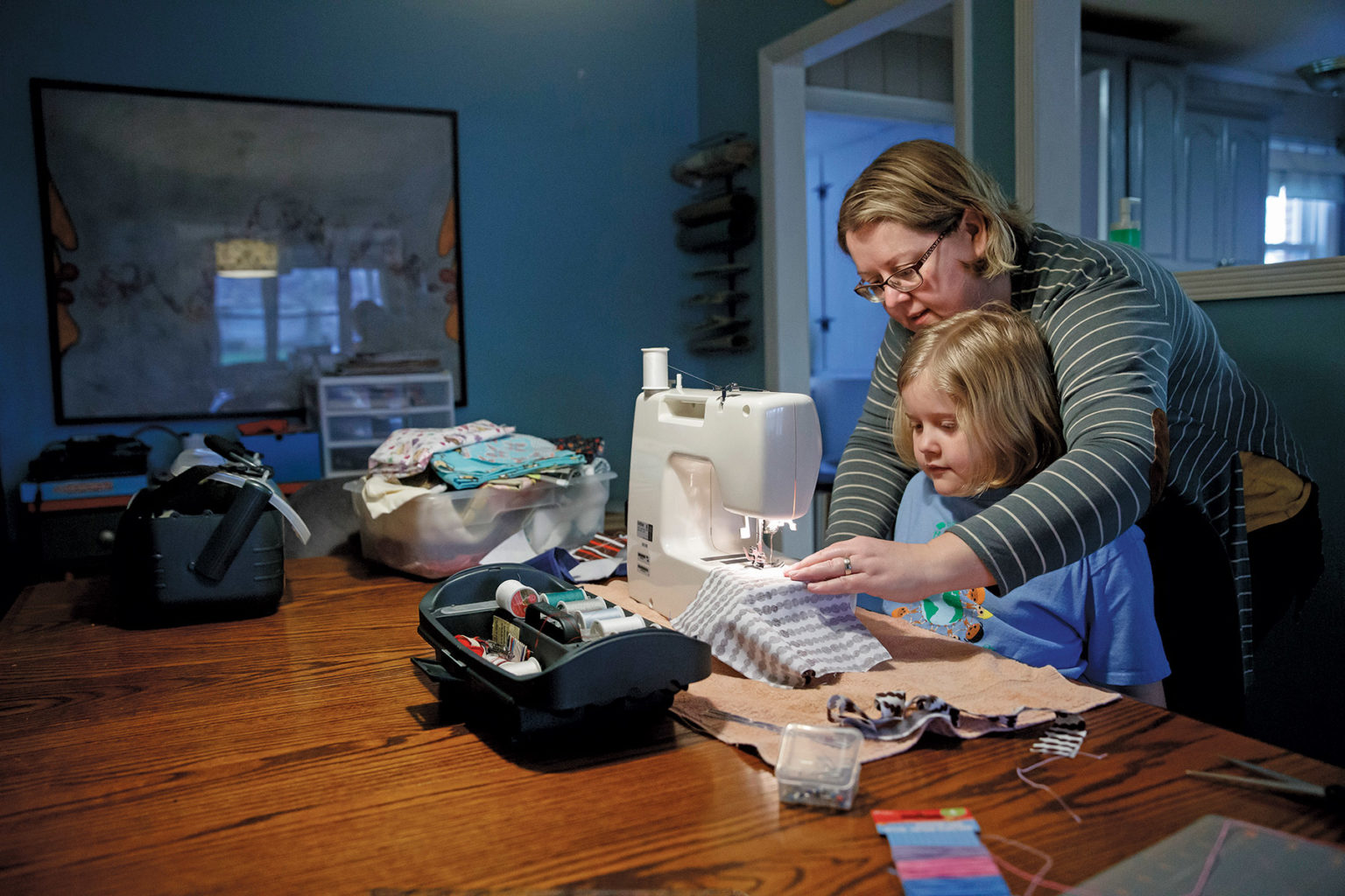 A mother and daughter work at a sewing machine making face masks