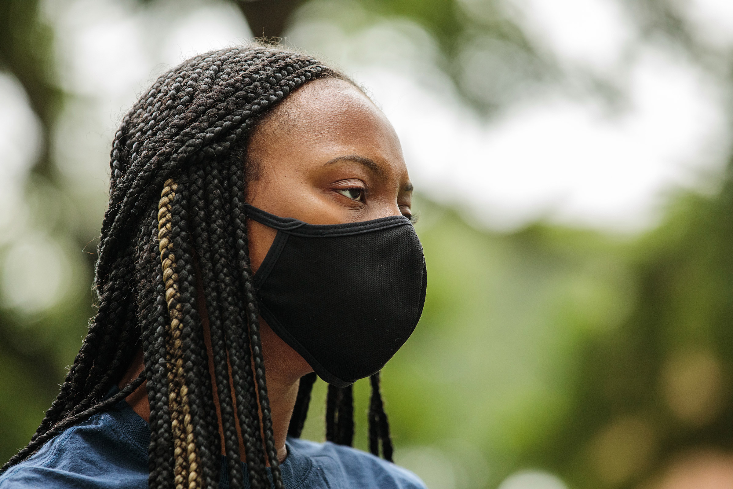 A young woman with braided hair speaks with her mask on