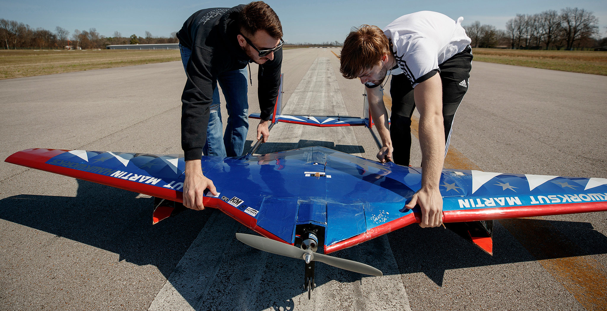 Two young men position a small aircraft on a test runway