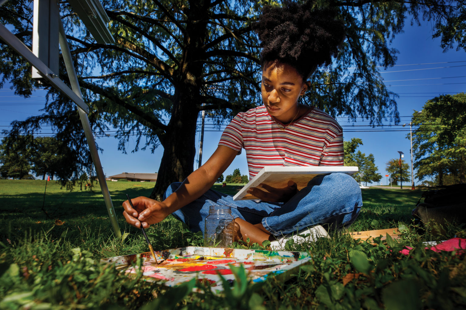 A Black woman sits under a tree and paints a canvas at UT Martin