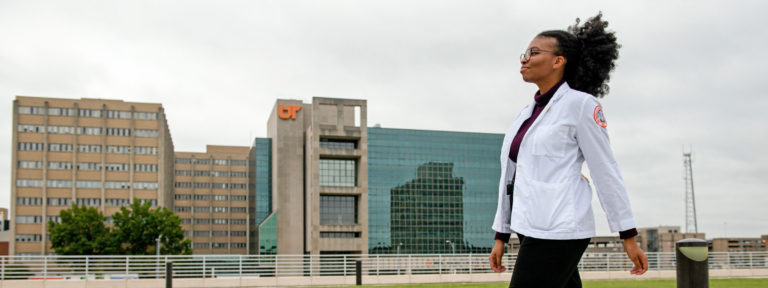 A Black woman in a white coat walks confidentally through the Memphis Medical District