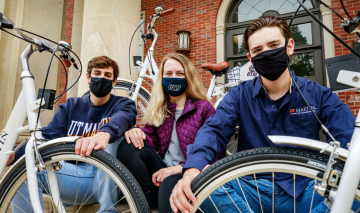 Three students wear face masks and grip their UTM bike tires