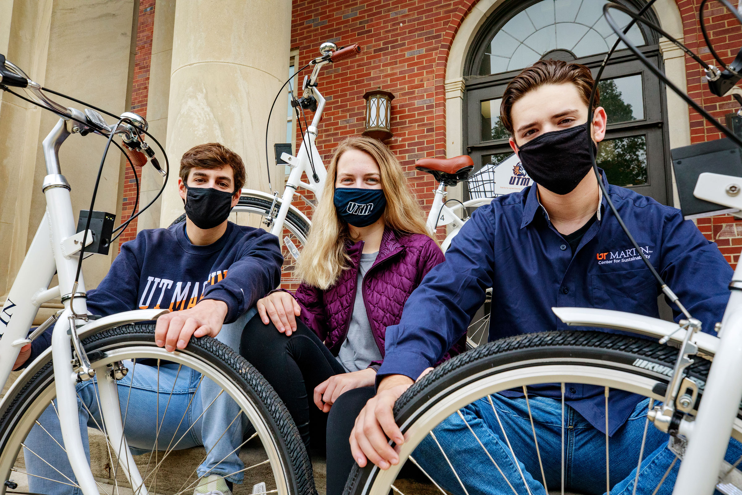 Three students wear face masks and grip their UTM bike tires