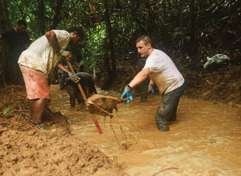 Two men dig out in a muddy trench