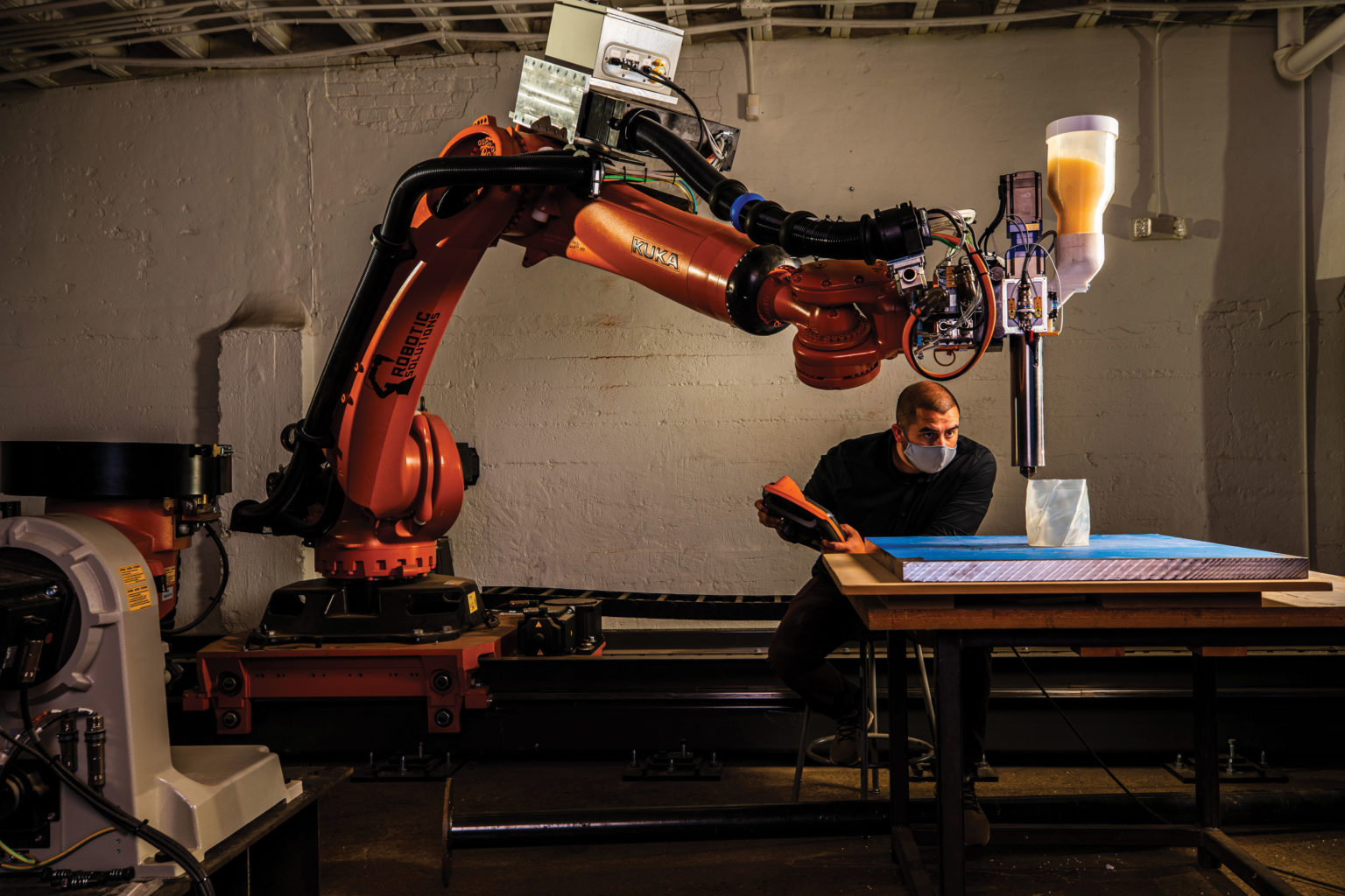 A large robotic arm fills a room while a man uses it to create a 3D prototype