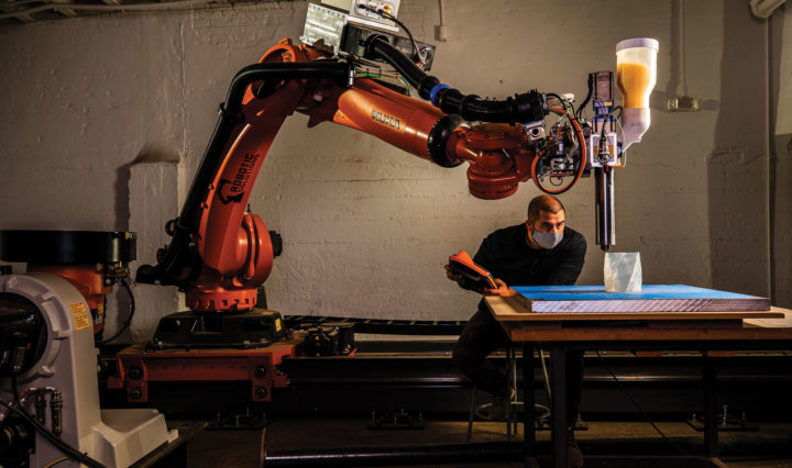 A large robotic arm fills a room while a man uses it to create a 3D prototype