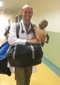 Ken Busby walks down a hospital corridor holding an infant practice mannequin
