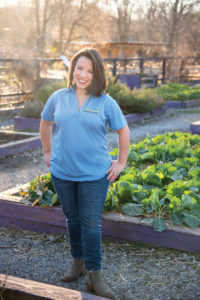 A woman in a UT Extension polo stands among the garden vegetables at the UT Gardens in Knoxville