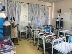 A nurse works in a neonatal intensive care unit, with two rows of small cribs and Mickey Mouse curtains