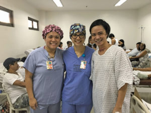 Two women in scrubs and a woman in a hospital gown stand for a photo together