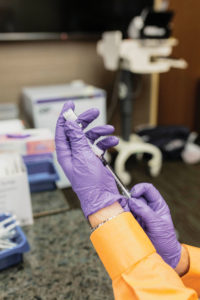 Brian Winbigler wears purple sterile gloves and prepares a vaccine