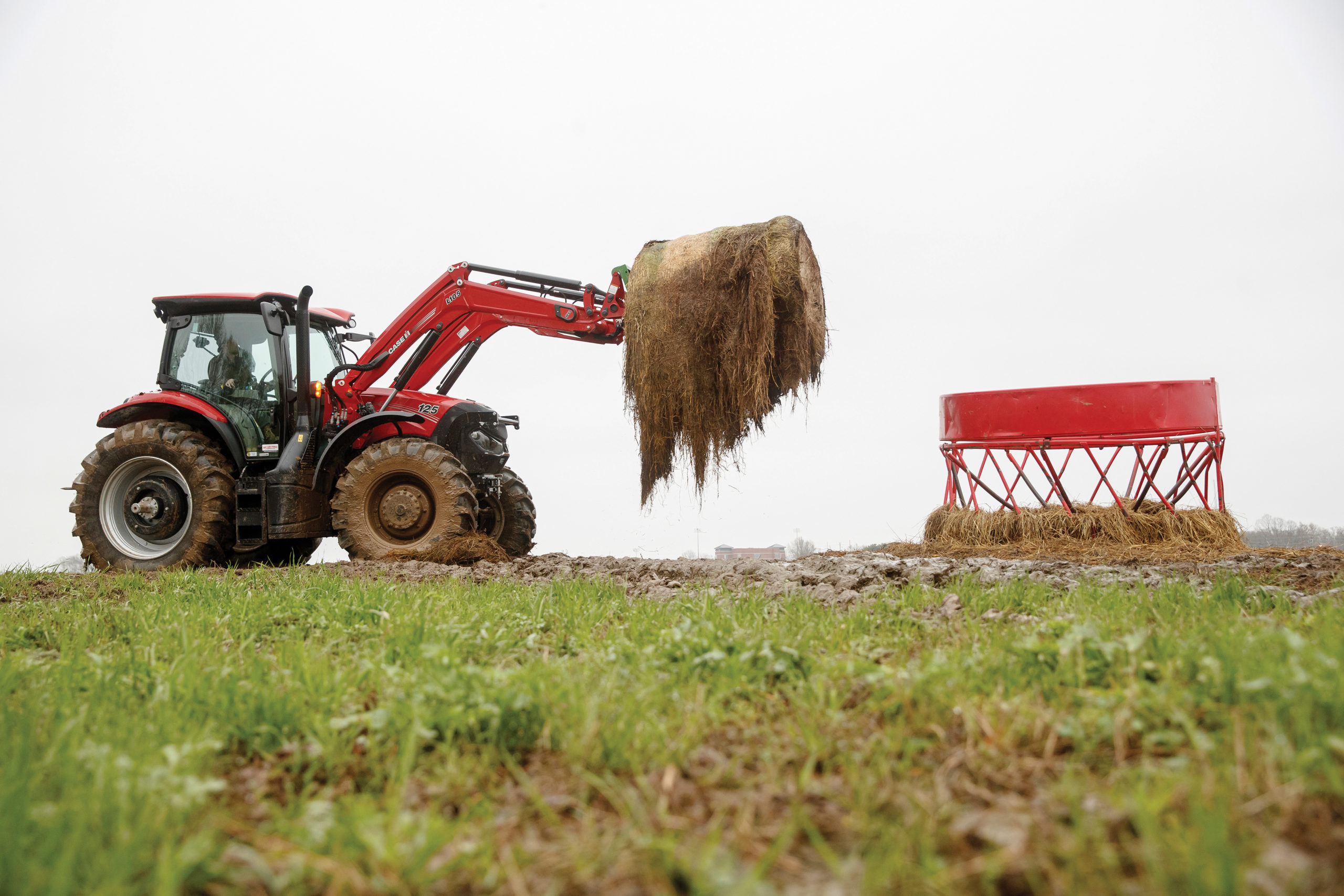 A red tractor lifts a large hay bale