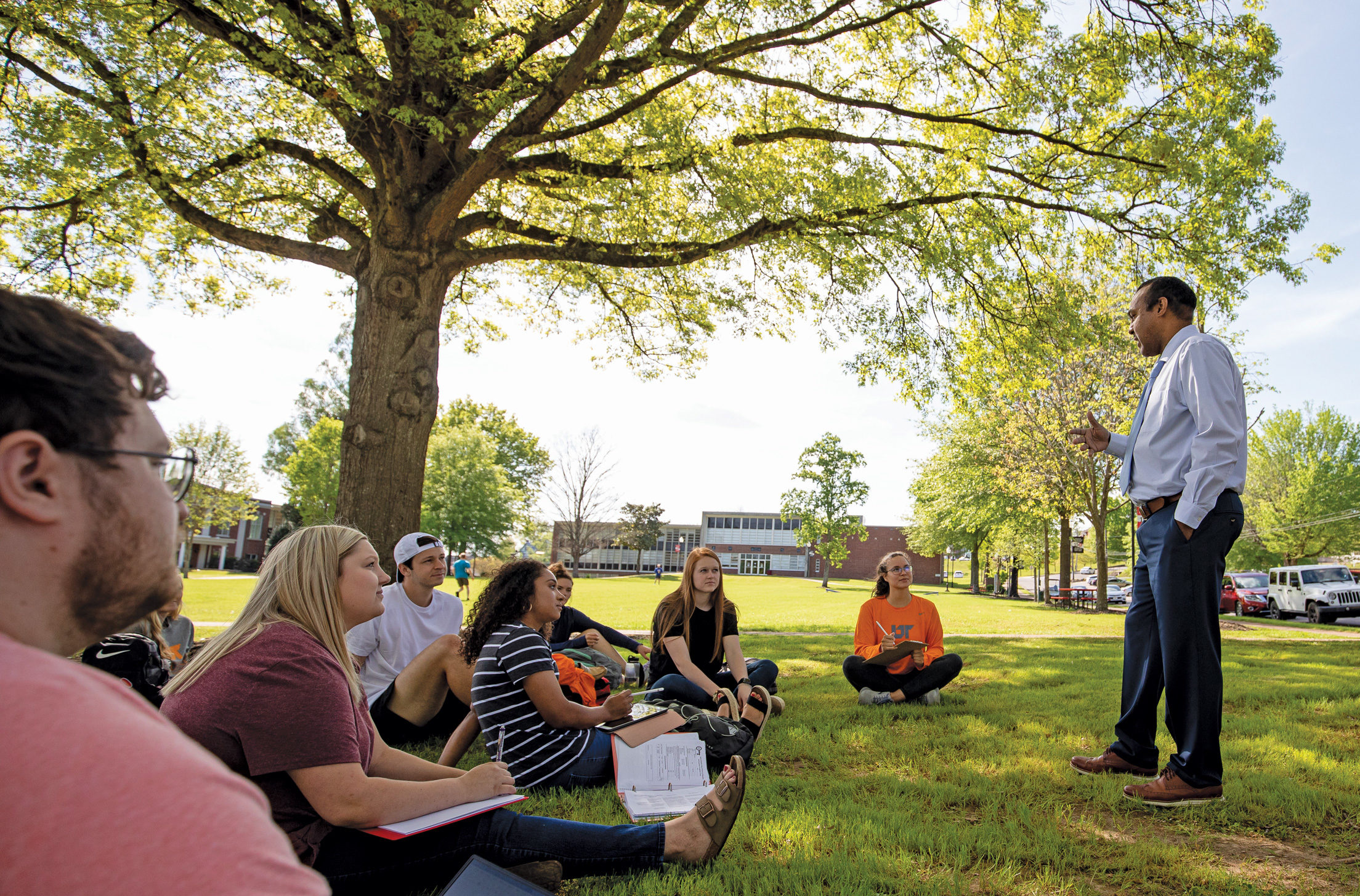 A professor delivers a lecture to his students seated on the lawn at UT Southern