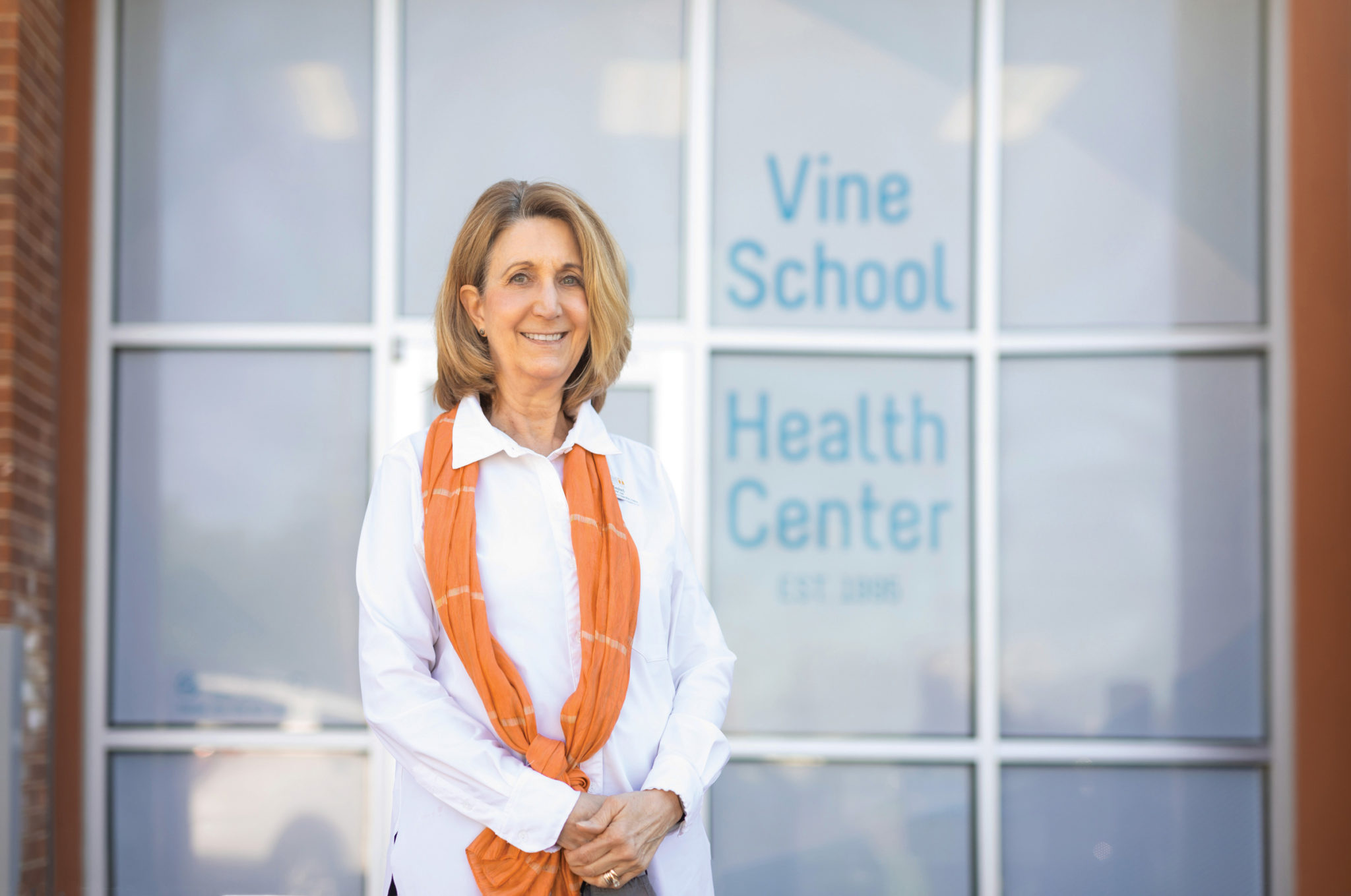 A middle aged woman stands outside the entrance to the Vine School Health Center