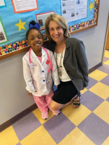 A little Black girl dressed as a nurse poses for a photo with a real-life nurse, a middle aged white woman in a colorful hallway