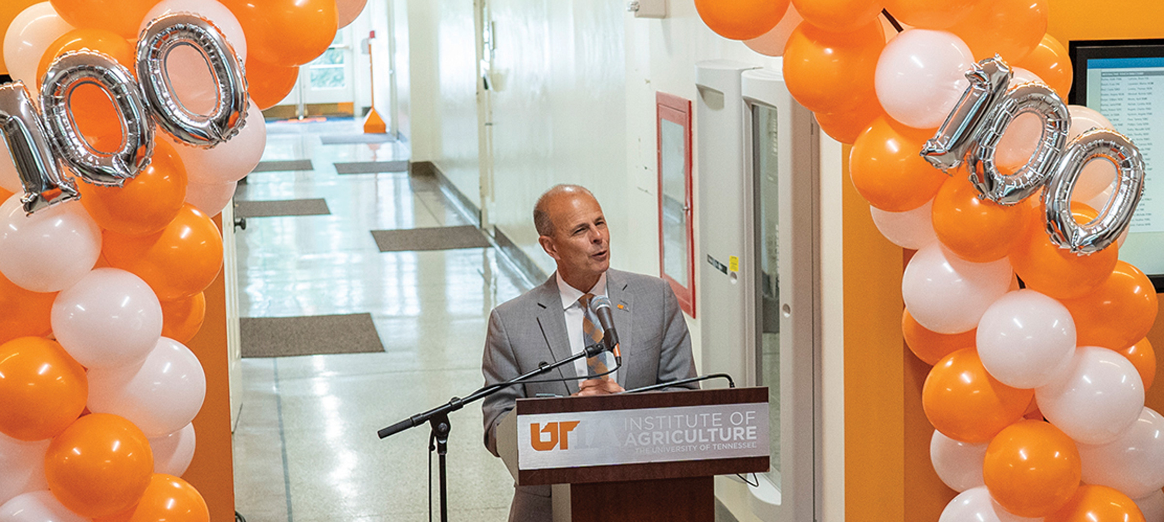 Tim Cross speaks at a podium surrounded by orange and white balloons