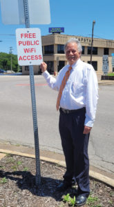 A middle aged white man stands next to a Free Public WiFi sign