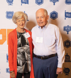 A senior couple pose in front of a backdrop of IPS agency logos