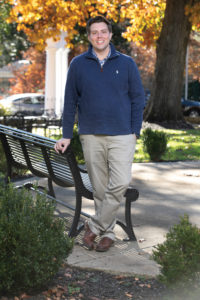 A man in a half zip sweater stands next to a park bench