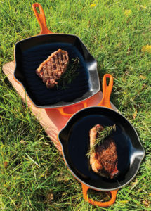 Two flank steaks in orange and black skillets