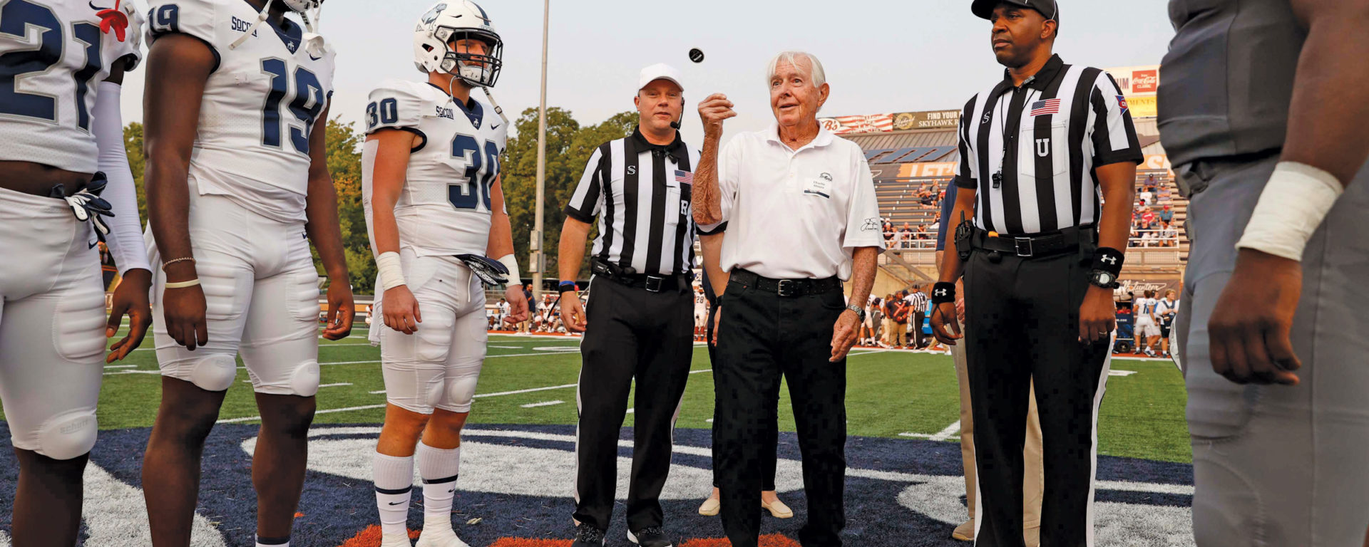 A man tosses a coin between two football referrees and captain of two teams
