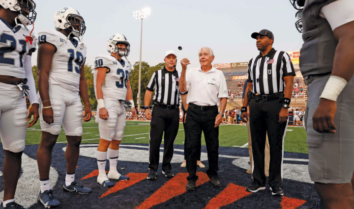 A man tosses a coin between two football referrees and captain of two teams