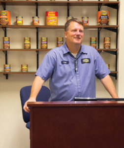 A man in Bush's Beans workshirt stands at a podium in front of Bush's products