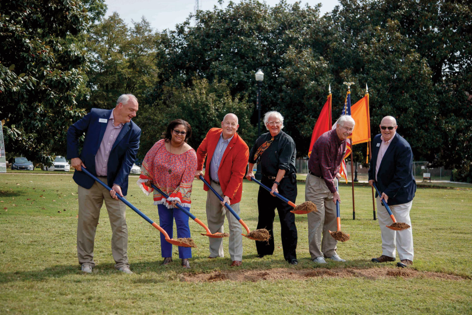 A group of people hold dirt in ceremonial blue and orange shovels at a groundbreaking
