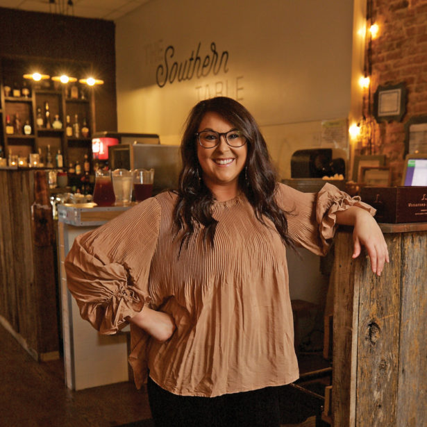 Keri Golden wearing designer frames and a pleated blouse, stands in the entrance of her restaurant