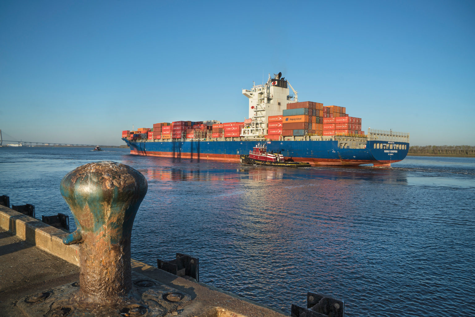 A large ship carries colorful container boxes on a clear sunny day
