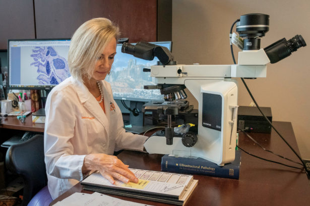 a woman in pearls and a white lab coat works at a microscope in her lab