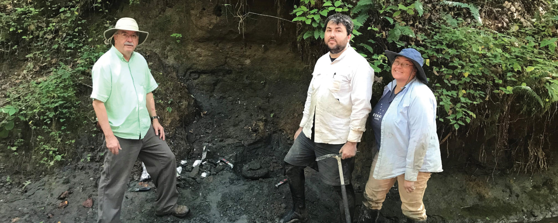 Three researchers stand in a creek bed looking for fossils
