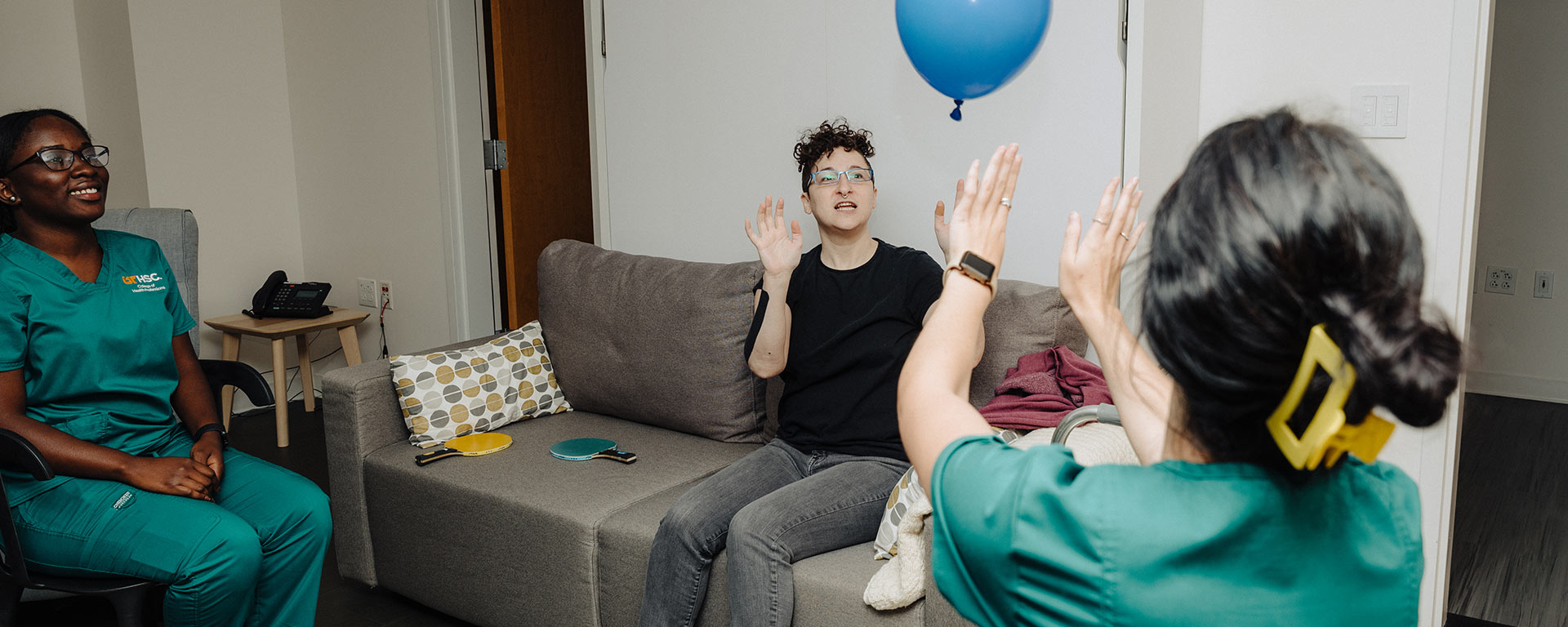 Occupational therapy student Akosua Odei watches as the actor playing a patient with multiple sclerosis bats a balloon with Georgia Ray, an occupational therapy student.