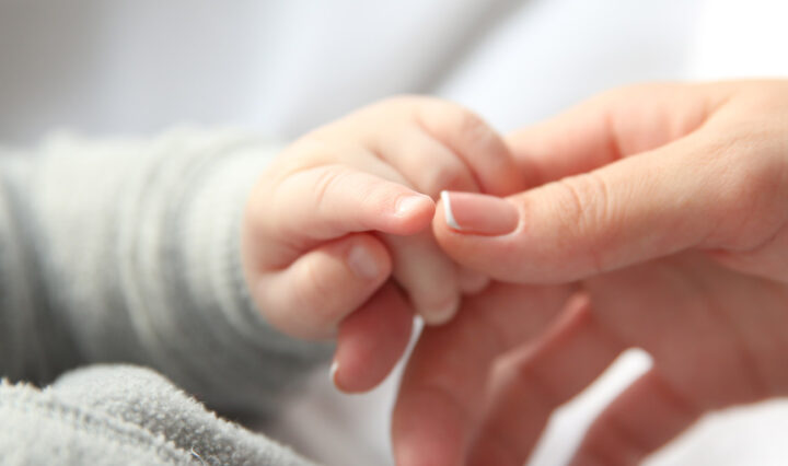 Close-up of infant grasping a woman's hand.