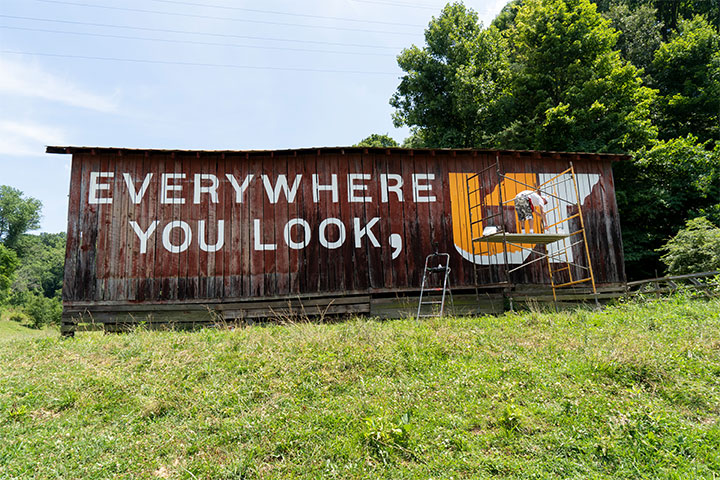 Everywhere You Look, UT mural being painted on the side of a barn next to Interstate 81 in Bristol.