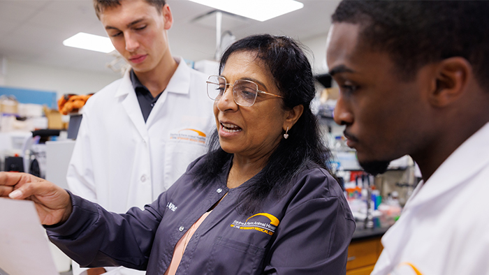 A female professor in a dark blue top discusses research with two male students.