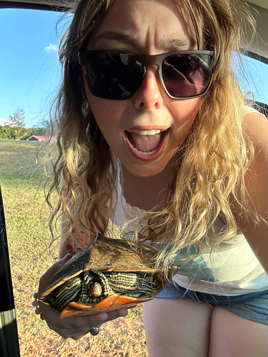 White female wearing sunglasses, holding a turtle.