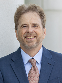 Headshot of an older white man, wearing a blue jacket and suit.