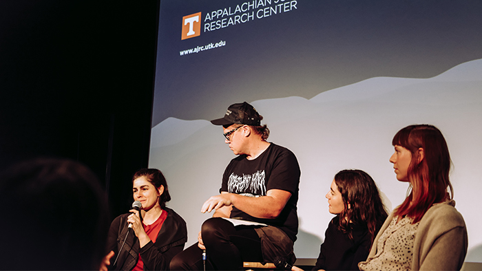 Four individuals sitting in front of a presentation screen.