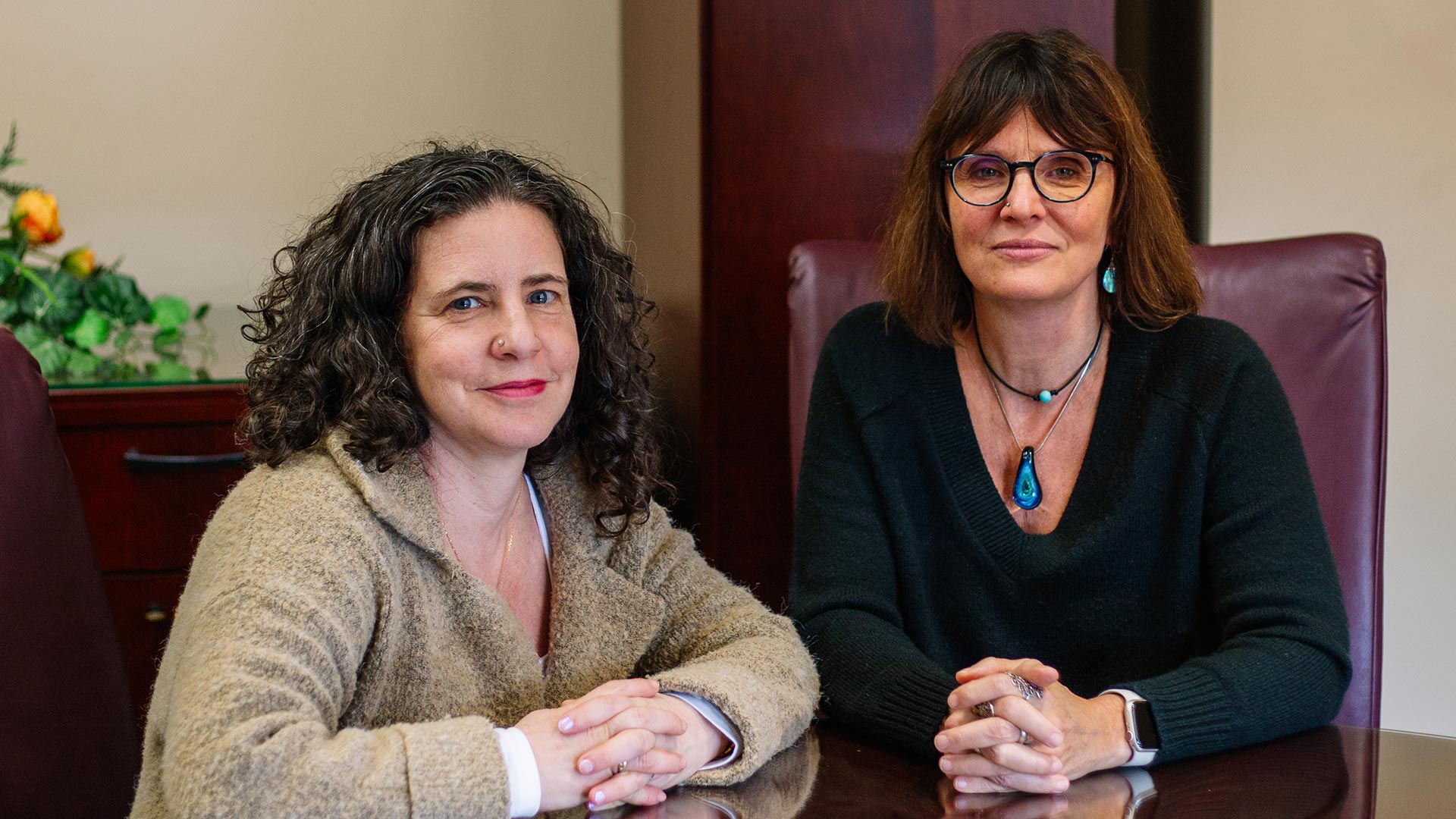 Two white women sitting at a table, hands clasped together.