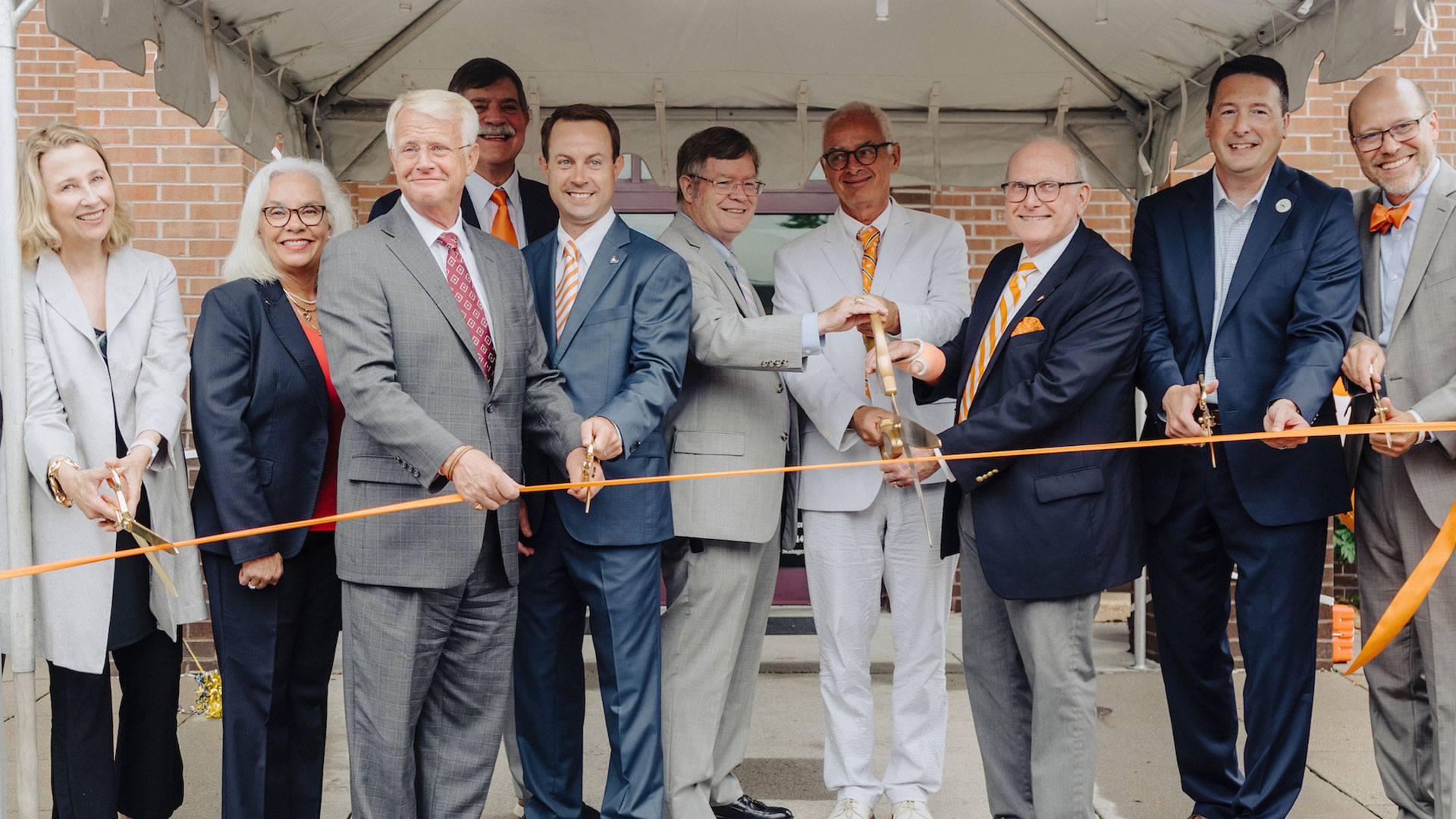 A group of men and women cutting a ceremonial orange ribbon.